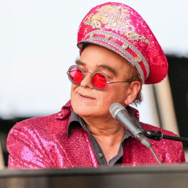 Elton John performing live on stage in a colorful outfit, showcasing his legendary music career and wealth