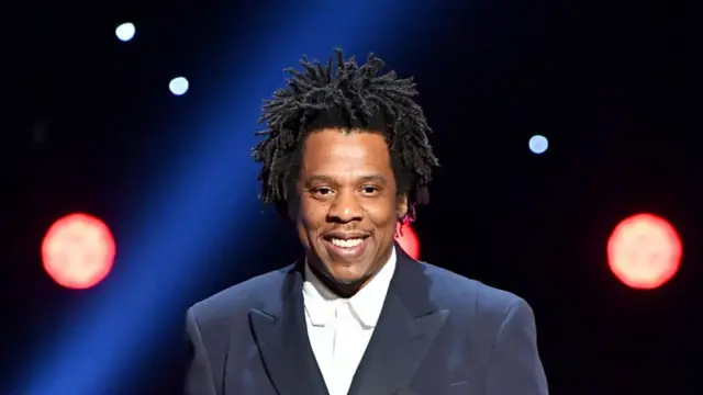 Jay-Z posing in a suit, symbolizing his billionaire status and success in music and business